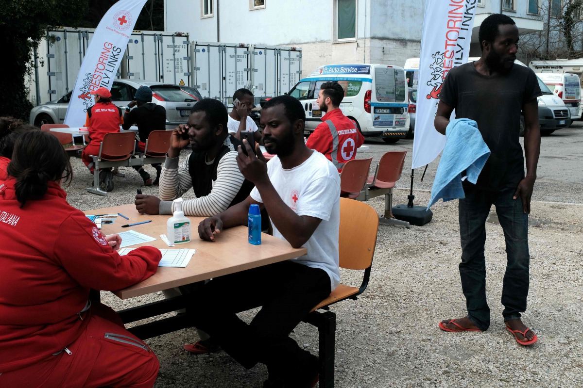 Migrants speak with members of the Italian Red Cross who help them to contact their family on March 6, 2017 outside the 