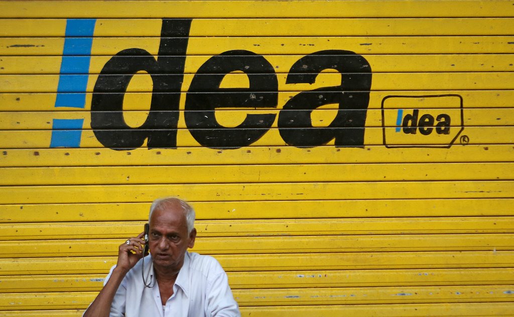 FILE PHOTO: A man speaks on his mobile phone as he sits in front of a shop displaying the Idea Cellular Ltd's logo on its shutter in Mumbai, India, April 28, 2014. Reuters/Danish Siddiqui
