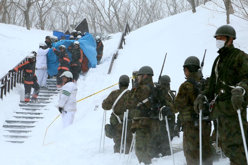 Firefighters carry a survivor they rescued from the site of an avalanche in Nasu town, Tochigi prefecture on March 27, 2017, while Self Defense Force personnel look on.  AFP / JIJI PRESS
