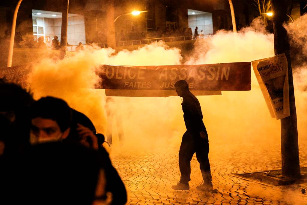 Anti riot police throws tear gas as a man stand next to a banner reading 
