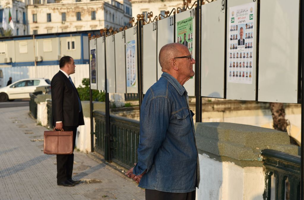 Algerian men look at electorial campaign posters for the upcoming legislative elections in Algiers' Martyrs Square as the official start of campaigning got underway on April 9, 2017. / AFP / RYAD KRAMDI / RYAD KRAMDI
