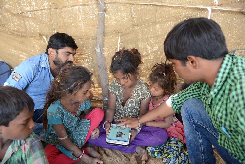 This picture taken on April 7, 2017 shows Anand Solanki (R), facilitator of the 'Zero Connect' programme, and teacher Deepsinh Vanola (top L), with a group of children of salt pan workers during a tent school workshop using an Internet-connected van, in t
