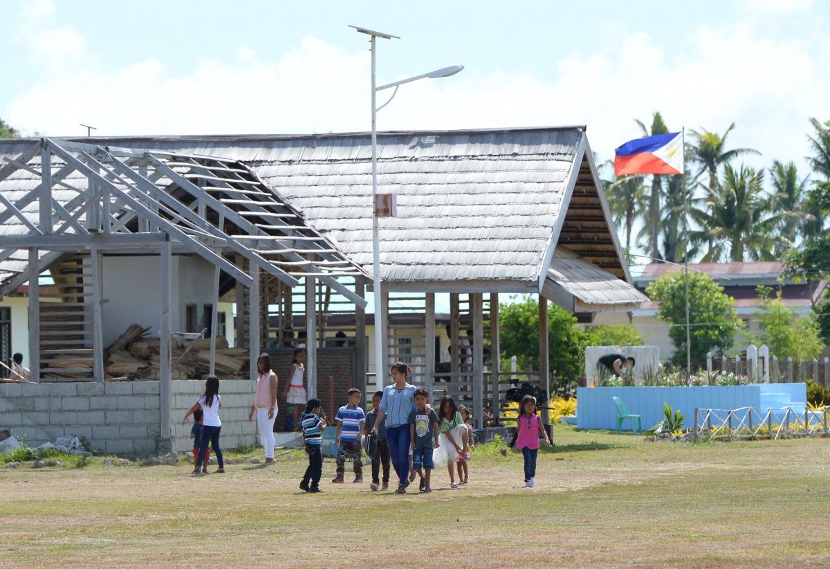 Students with their teacher walk past a flag near the airport, during the visit of Defence Secretary Delfin Lorenzana to the Philippine-claimed island Thitu in The Spratlys on April 21, 2017. AFP / Ted Aljibe
