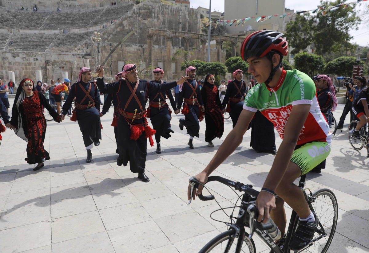 A cyclist rides past a group of traditional dancers at the ancient Roman theatre in the centre of Amman during a welcome ceremony for members of the Middle East Peace Tour pre-Event on April 24, 2017. AFP / Menahem Kahana