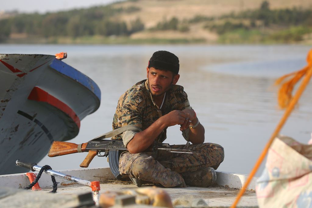A member of the US-backed Syrian Democratic Forces (SDF), made up of an alliance of Arab and Kurdish fighters, sits on the edge of a boat at the Tabqa dam on April 29, 2017. AFP / DELIL SOULEIMAN