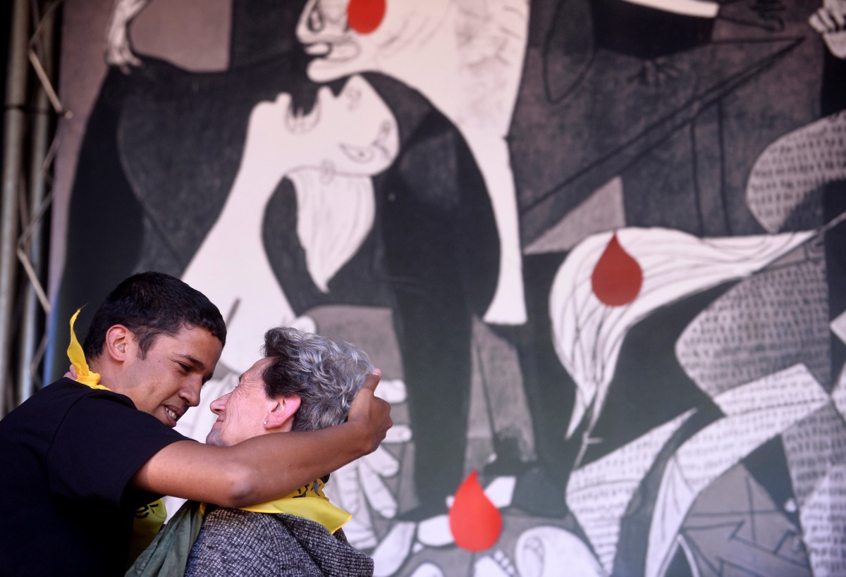 Refugee resident in Spain, Hassanna Aailia, from Western Sahara embraces Pilar Ostolaza, refugee in France during the Spanish Civil War, in front of a reproduction of Picasso's Guernica during the Ongi Etorri Errefuxiatuak (Welcome Refugees) rally in the 