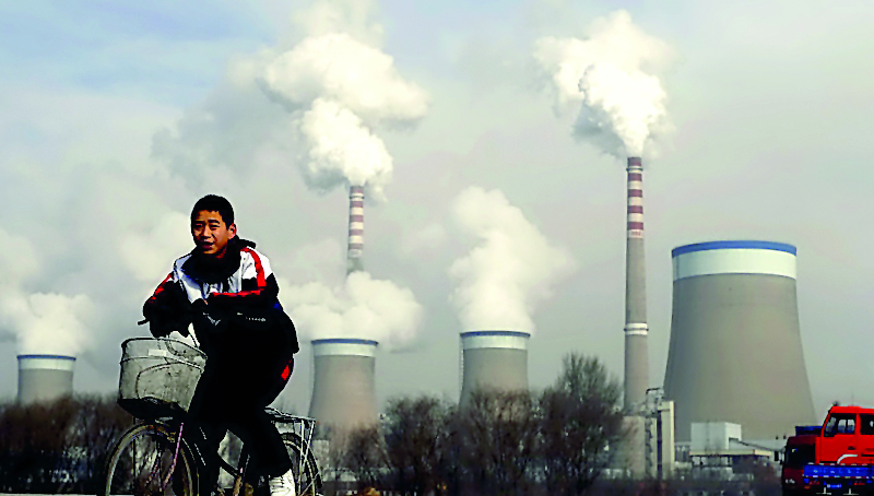 A Chinese boy cycles past a cooling towers of a coal-fired power plant in Dadong, Shanxi province, China, in this file photo.