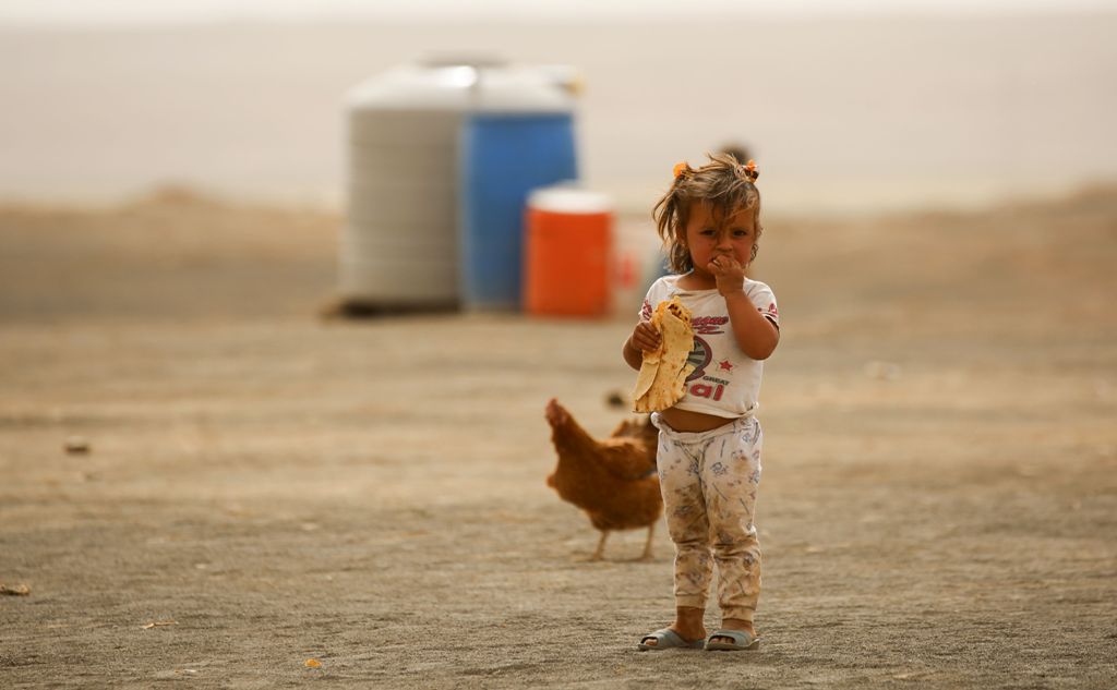 A displaced child, who fled from the Islamic State (IS) group bastion of Raqa, stands outside as she eats a loaf of bread in a camp for displaced near the town of al-Karamah, 26 kms from Raqa, on May 10, 2017. / AFP / DELIL SOULEIMAN