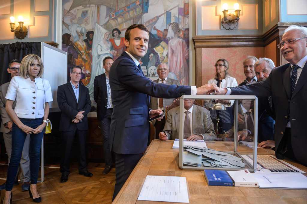 French President Emmanuel Macron (C) casts his ballot next to his wife Brigitte Macron (L) at a polling station during the first round of the French legislative elections in Le Touquet, on June 11, 2017. / AFP.