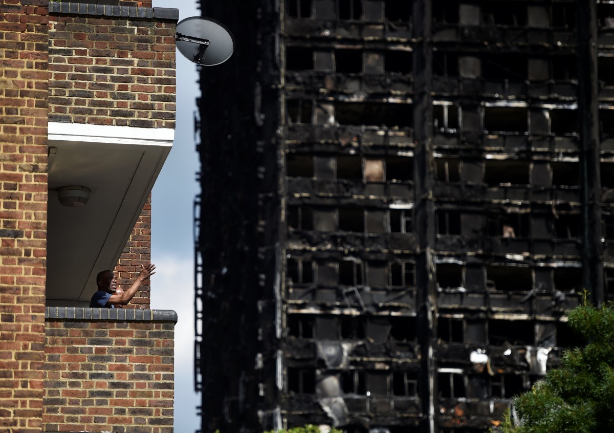 A man stands on his balcony in front of the burnt out shell of the Grenfell apartment tower block in North Kensington, London, Britain, June 17, 2017. REUTERS/Hannah McKay
