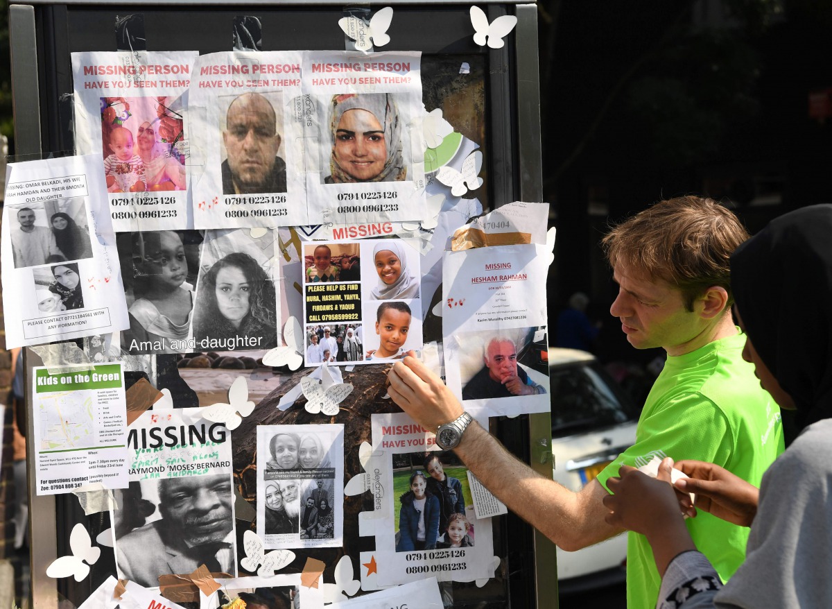 People look at images of missing people, placed on a phone box near to the Grenfell Tower, a residential tower block in Kensington, west London, on June 19, following the June 14 fire which gutted the residential building. (AFP / Paul ELLIS)