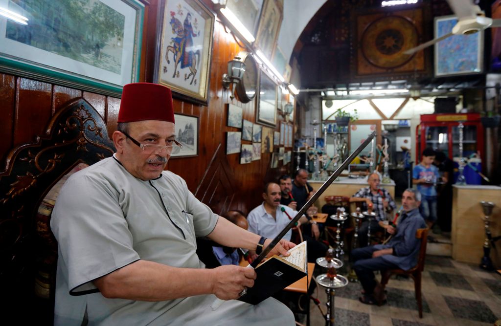 Ahmad al-Lahham, a Syrian storyteller, reads from his storybook in a Damascus coffeehouse on June 19, 2017. AFP / LOUAI BESHARA
