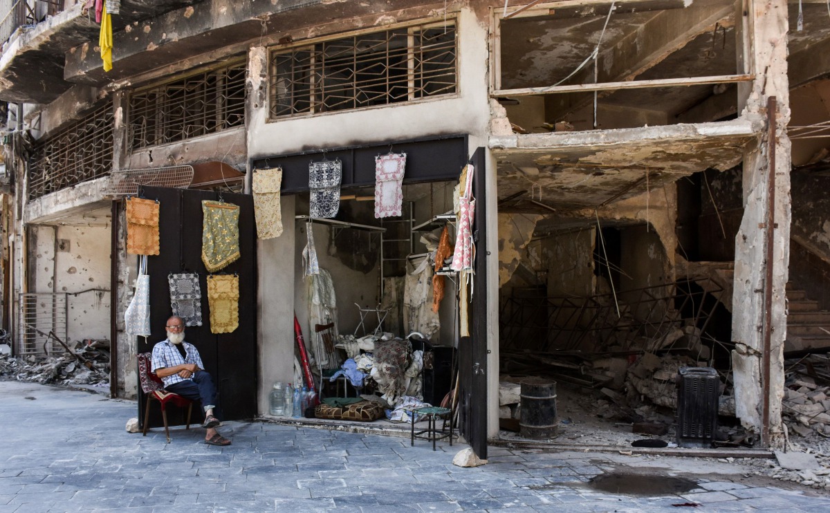 An elderly Syrian sits outside a newly-reopened shop amid the destruction, where he sells tablecloths in the old city of Aleppo on July 22, 2017. (AFP / George OURFALIAN)