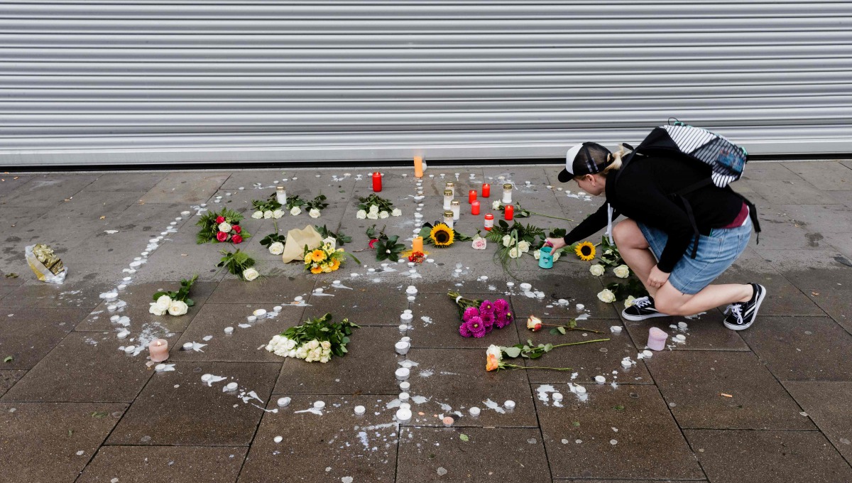 A woman places a candle at a makeshift memorial of flowers and candles arranged like a peace sign on July 29, 2017 in Hamburg, northern Germany, at the site where a man killed one person and wounded several others in a knife attack the day before. (AFP / 