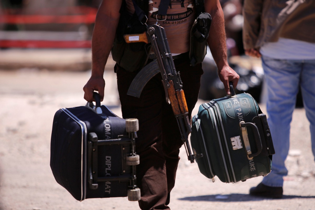 A rebel fighter carries suitcases and his weapon prior to boarding a bus as rebel fighters the besieged Waer district in the central Syrian city of Homs, May 21, 2017. (REUTERS / Omar Sanadiki) 