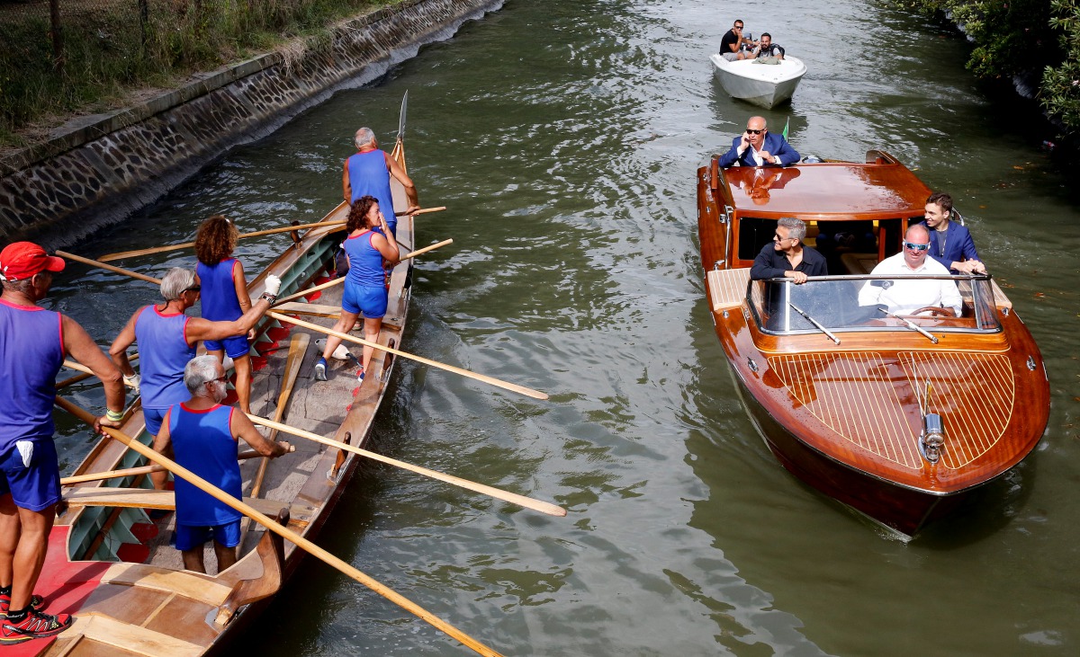 Actor George Clooney (L) is greeted by a boat crew as he arrives for the movie 