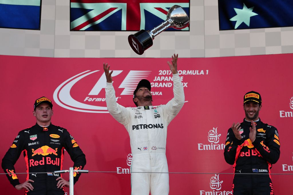 Mercedes' British driver Lewis Hamilton (C) throws his winner's trophy as second placed Red Bull's Dutch driver Max Verstappen (L) and Red Bull's Australian driver Daniel Ricciardo (R) look on from the podium in the Formula One Japanese Grand Prix at Suzu