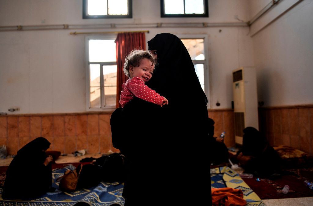 The wife of a suspected member of the Islamic State (IS) group holds her child as she waits on the western frontline to be questioned after fleeing the centre of Raqa, on October 8, 2017.  AFP / BULENT KILIC
