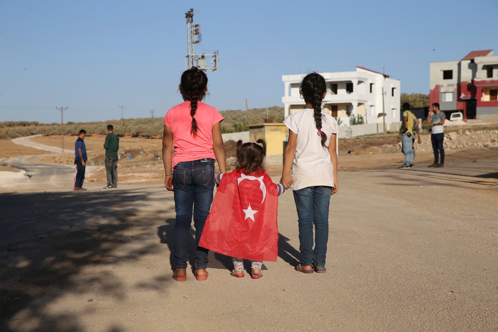 Children hold hands of a little girl wearing a Turkish flag during Turkish Army's armoured vehicles' deployment to the border line in the Turkish border district of Reyhanli near Syria's Idlib, within the reconnaissance activities in Idlib as part of an i