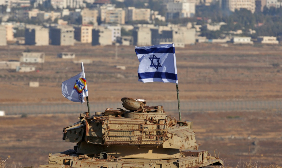 An Israeli flag flutters above the wreckage of an Israeli tank sitting on a hill in the Israeli-occupied sector of the Golan Heights and overlooking the border with Syria and the town of Quneitra, on October 18, 2017.  AFP / Jalaa Marey