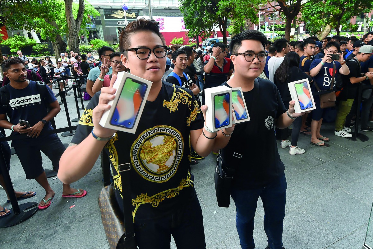 The first customers to purchase their new iPhone X smartphone pose outside an Apple store during its launch in Singapore on November 3, 2017. AFP / Roslan Rahman