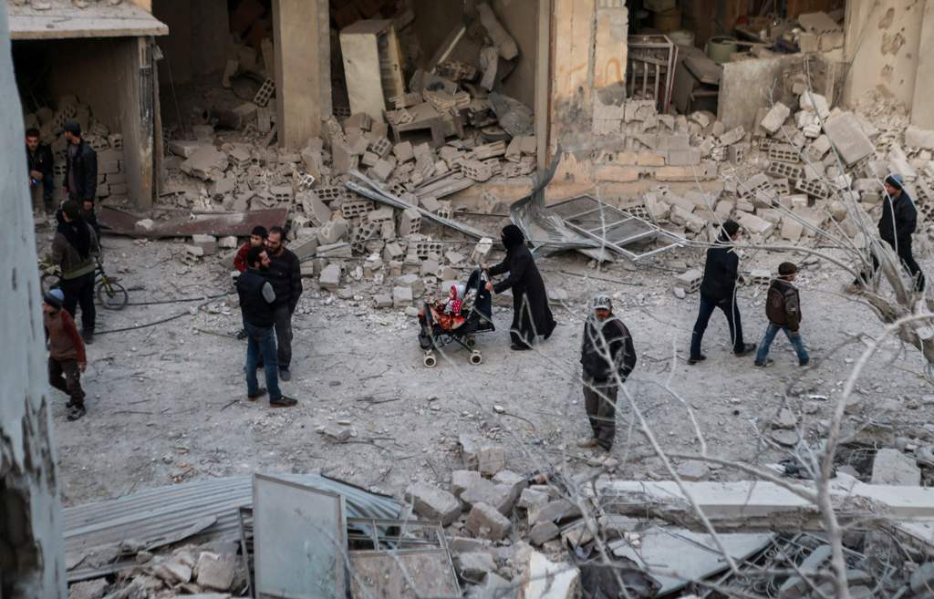 Syrians walk through the rubble down a street filled with destroyed buildings, in the aftermath of reported bombardment by government forces in the rebel-held besieged town of Arbin, in the Eastern Ghouta region on the outskirts of Damascus, during an air