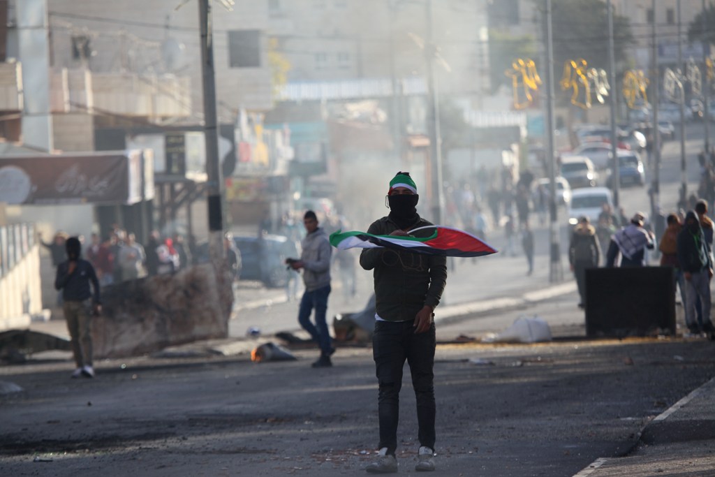A Palestinian holds a Palestinian flag as Israeli security forces intervene in a demonstration against U.S. President Donald Trump's recognition of Jerusalem as Israel's capital, in Bethlehem, West Bank on December 10, 2017. ( Mamoun Wazwaz - Anadolu Agen