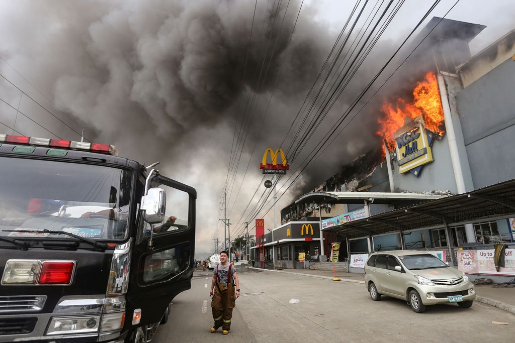 This photo was taken on December 23, 2017, shows a firefighter standing in front of a burning shopping mall in Davao City on the southern Philippine island of Mindanao.  AFP / MANMAN DEJETO

