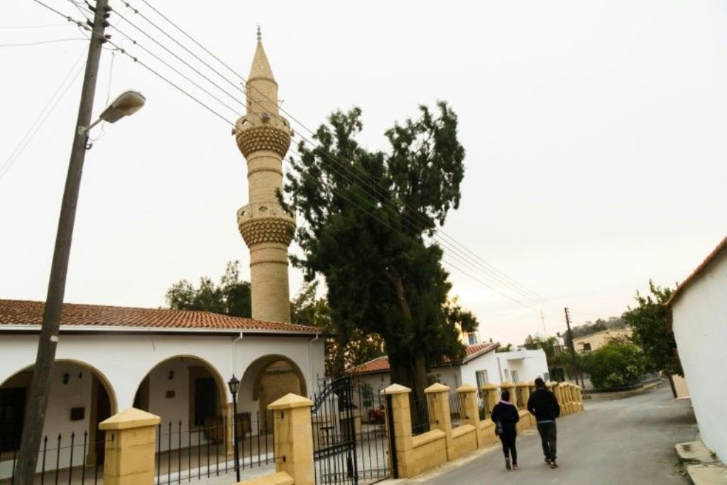 A couple walks past a mosque in the mixed village of Pyla, which lies in the UN-patrolled buffer zone that slices across the island of Cyprus. Clement Melki / AFP
