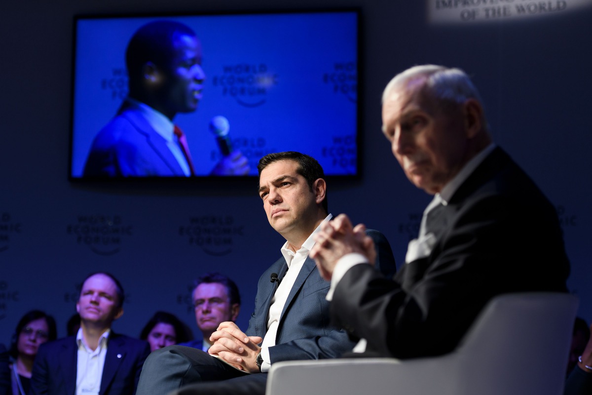 Greek Prime Minister Alexis Tsipras (C) and Organization for Migration (IOM) Director-General William Lacy Swing listen a refugee seen on TV screen behind during a session on mass migration across the Mediterranean during the annual World Economic Forum (