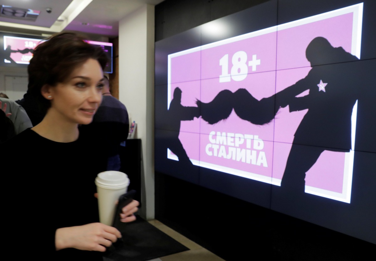 A woman walks past a monitor displaying the 