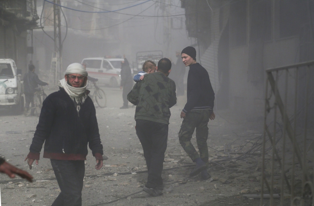 An elderly Syrian man carries a child as he walks through the dust following a reported regime air strike in the rebel-held town of Hamouria, in the besieged Eastern Ghouta region on the outskirts of the capital Damascus, on February 6, 2018. / AFP / ABDU