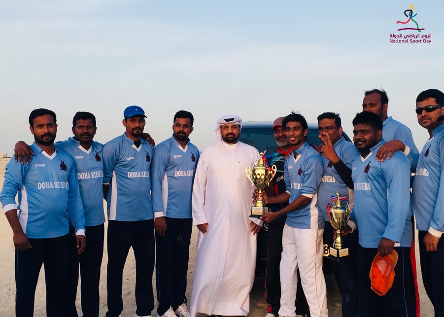 Doha Riders winners of the National Sport Day four-team cricket tournament pose for a picture with an official.