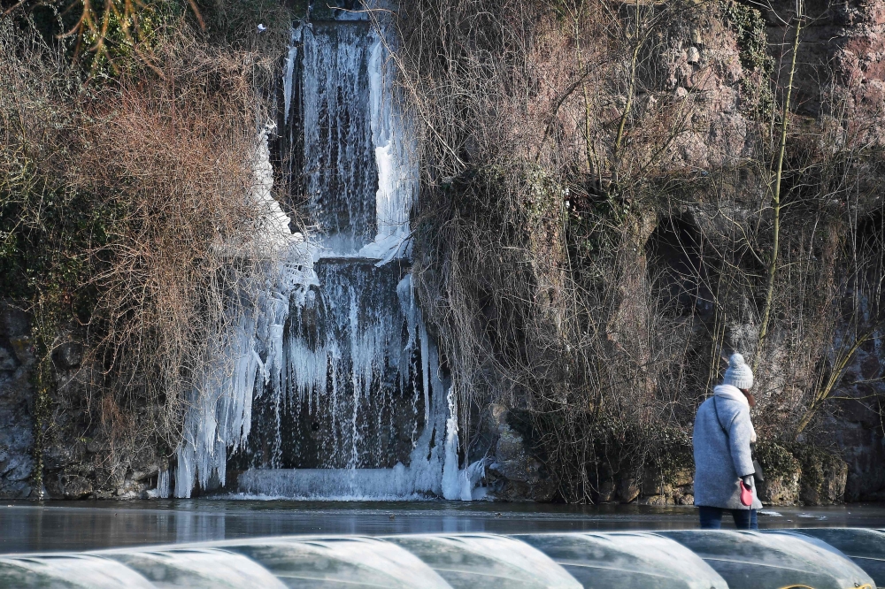 A pedestrian walks past a frozen waterfall hanging above a lake in The Orangerie Park in Strasbourg, eastern France on February 27, 2018. AFP / FREDERICK FLORIN