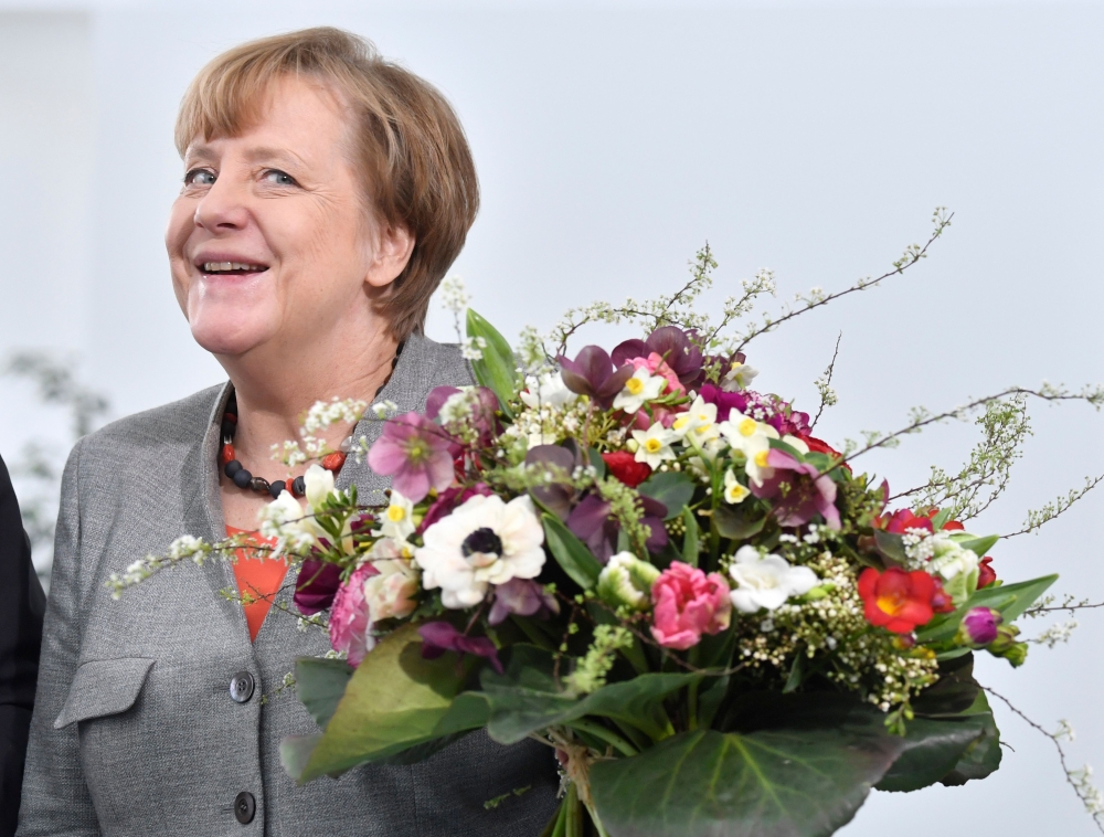 (FILES) This file photo taken on February 9, 2018 shows German Chancellor Angela Merkel holding a flower bouquet given to her by the President of the German Horticultural Association in the chancellery in Berlin.  AFP / John MACDOUGALL
