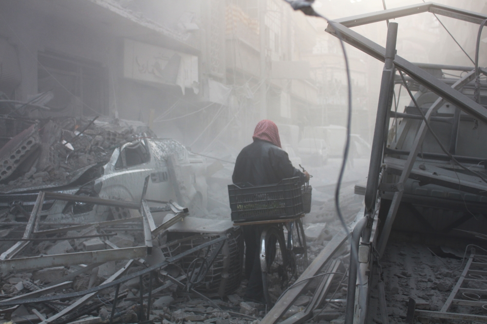 A Syrian walks with his bicycle amid debris of buildings after Assad Regime's airstrike hit residential areas in Eastern Ghouta's Douma town despite decisions to implement a ceasefire made separately by Russia and the UN Security Council, in Damascus, Syr