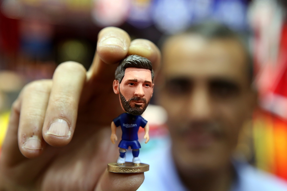 A sports shop keeper holds a figurine of Argentine football player Lionel Messi at a shop in Kuwait City on April 11, 2018, as Spain’s Real Madrid and Italy’s Juventus prepare to play for second leg of Europe Champions league quarter finals. AFP / Yasser 