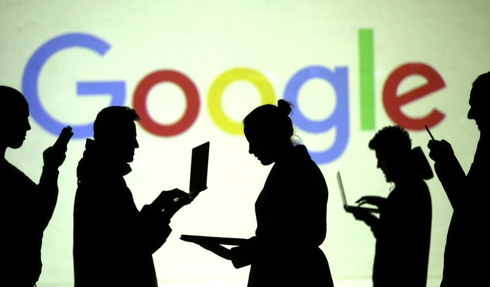 Silhouettes of laptop and mobile device users are seen next to a screen projection of Google logo in this picture illustration taken March 28, 2018. Reuters/Dado Ruvic