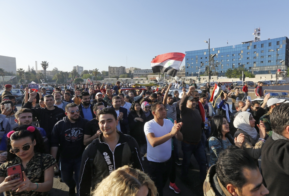 Syrians wave the national flag and wave portraits of President Bashar al-Assad as they gather at the Umayyad Square in Damascus on April 14, 2018, to condemn the strikes carried out by the United States, Britain and France against the Syrian regime. AFP /
