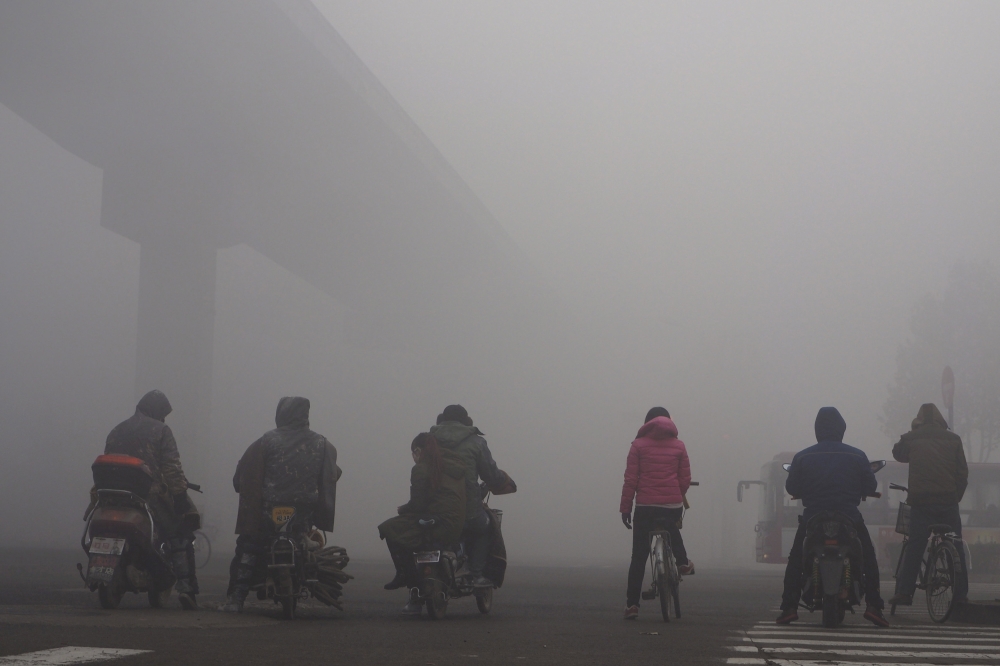 FILE PHOTO: Residents on their bicycles and electric bikes wait for the traffic at an intersection amid heavy smog in Shijiazhuang, Hebei province, China, December 10, 2015. REUTERS/Stringer/File Photo
