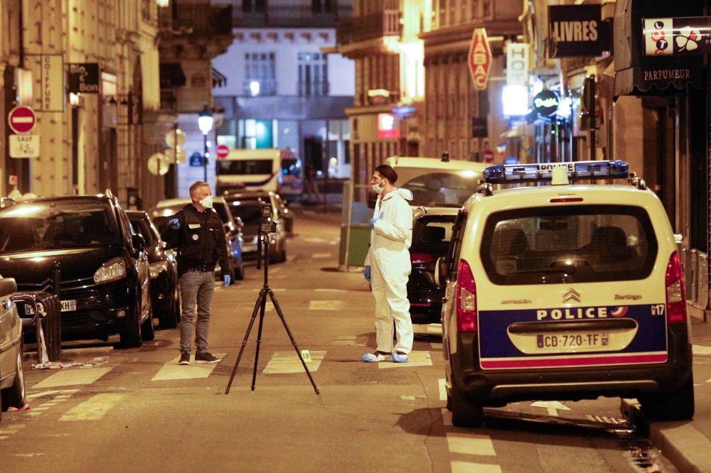 A forensic officer (R) and a French policeman (L) stand next to a numbered reference index pad and a camera on a tripod on Saint Augustin street in Paris after one person was killed and several injured by a man armed with a knife, who was shot dead by pol