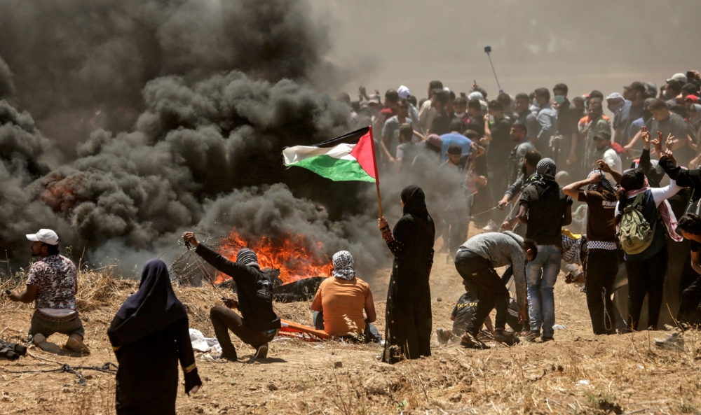A Palestinian woman holding her national flag looks at clashes with Israeli forces near the border between the Gaza strip and Israel east of Gaza City on May 14, 2018, as Palestinians protest over the inauguration of the US embassy following its controver