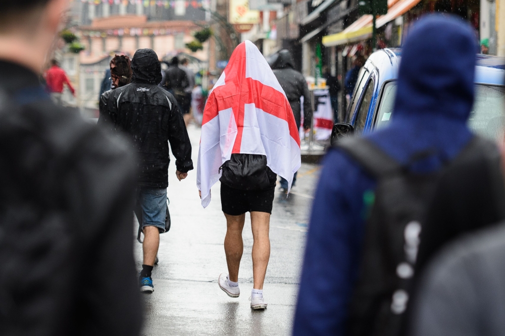 (FILES) In this file photo taken on June 16, 2016, a football supporter covers his head with an England flag, the St George's Cross, as he walks in the rain in Lens, northern France, on the day England played against Wales in their Euro 2016 group B footb
