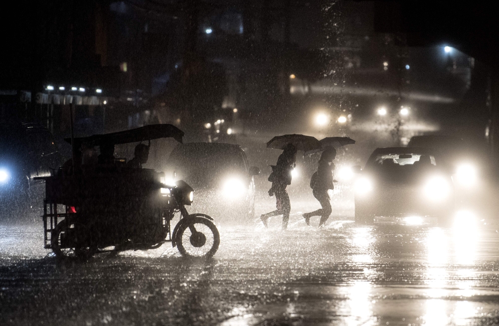 People cross a road during heavy rain caused by Typhoon Maliksi in Manila on June 10, 2018. AFP / Noel Celis