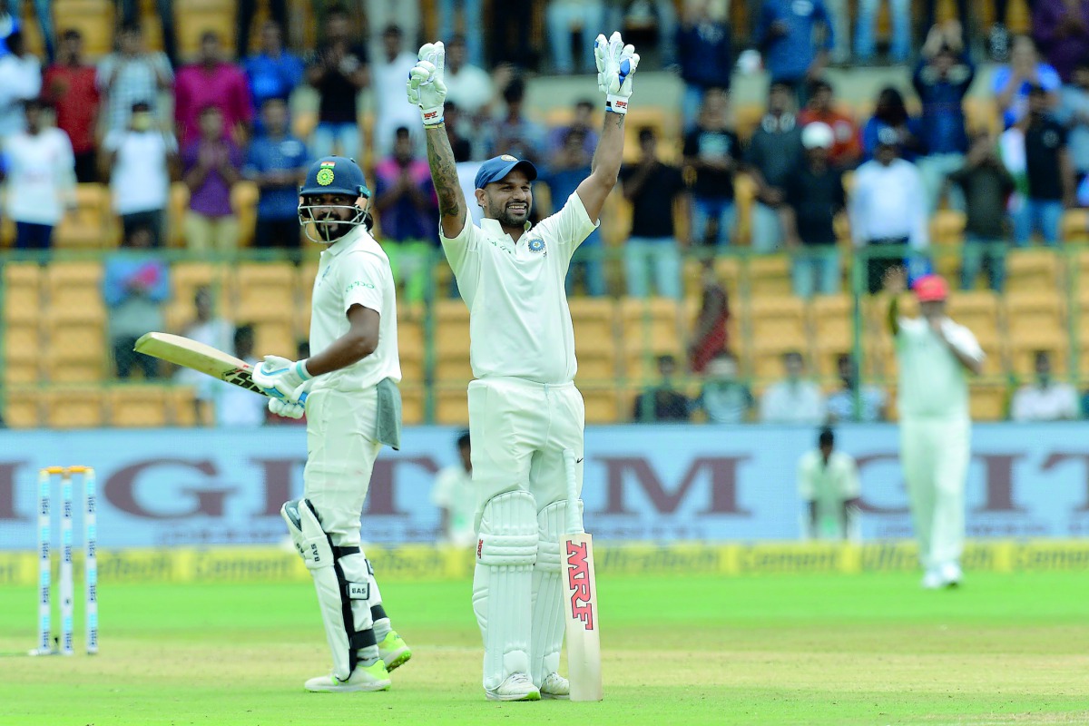 Indian cricketer Murali Vijay (L) looks on as teammate Shikhar Dhawan (C) celebrates his century (100 runs) during the first day of the one-off cricket Test match between India and Afghanistan at The M. Chinnaswamy Stadium in Bangalore on June 14, 2018. A