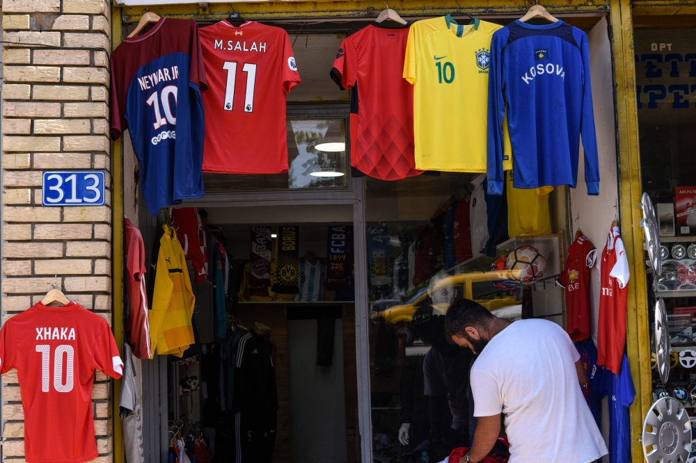 This photograph taken, shows a Kosovo Albanian pedestrian walking past a replica football jersey of Switzerland's midfielder Granit Xhaka outside a shop in the Kosovo capital Pristina. Football-fever among Kosovans for the World Cup has skyrocketed as thr