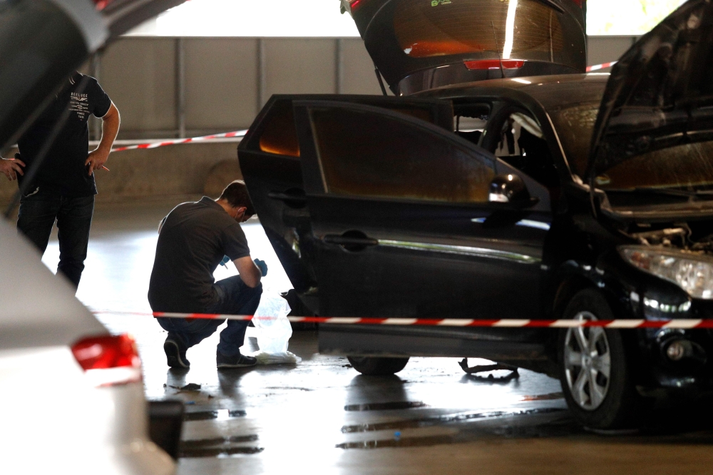 This picture taken on July 1, 2018 in Aulnay-sous-Bois, north of Paris shows a forensic police officer investigating a car abandoned by French armed robber Redoine Faid at O'Parinor shopping mall parking after his escape onboard a helicopter from a prison