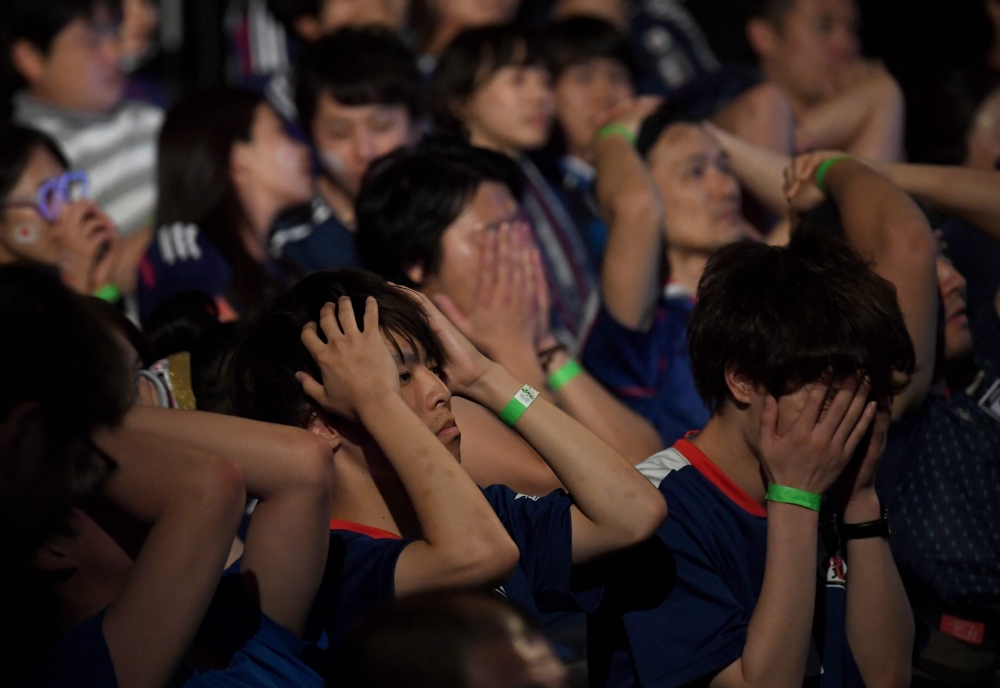 Japanese soccer fans react while watching Japan's loss to Belgium in a public viewing of the 2018 Russia World Cup round of 16 football match in Tokyo early July 3, 2018. / AFP / Toshifumi Kitamura 