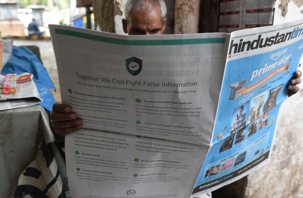 This photo illustration shows an Indian newspaper vendor reading a newspaper with a full back page advertisement from WhatsApp intended to counter fake information, in New Delhi on July 10, 2018.  AFP / Prakash Singh