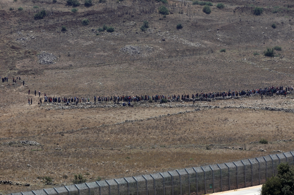 People start to walk away from the border fence between Israel and Syria at its Syrian side as it is seen from the Israeli-occupied Golan Heights near the Israeli Syrian border July 17, 2018. REUTERS/Ronen Zvulun